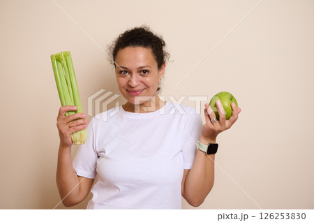 Smiling Woman Holding Fresh Green Apple and Celery Stalks Promoting Health and Wellness 126253830