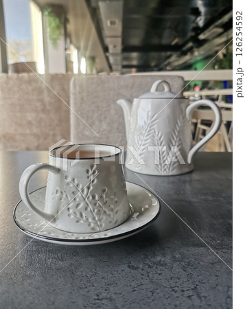 A white ceramic teacup with matching teapot on a modern table in a stylish cafe interior. 126254592