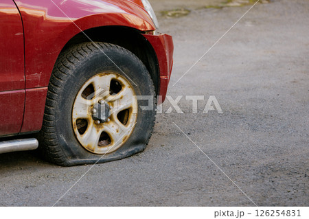 red car with a flat tire is parked in front of the house. An old wrecked car was abandoned. 126254831