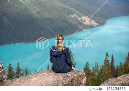 Tourist sitting on a rock ledge overlooking Peyto Lake in Banff National Park, Canada. 126254853
