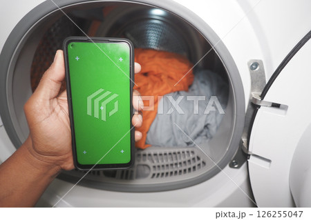 Hand with smartphone by dryer and colorful laundry 126255047