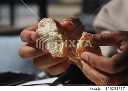 Hands breaking apart freshly baked bread in a sunny cafe Hands breaking apart freshly baked bread in a sunny cafe 126255217