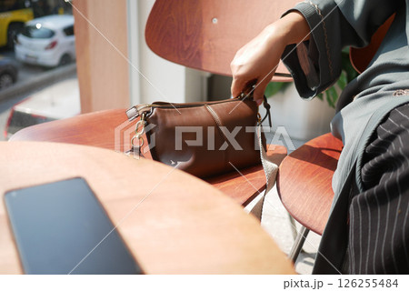 A person adjusts belongings in a brown bag at a sunlit cafe table A person adjusts belongings in a brown bag at a sunlit cafe table 126255484