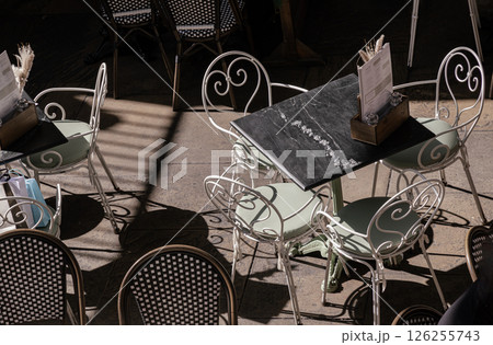 Victorian style openwork white metal chairs and square marble table outside cafe area. 126255743