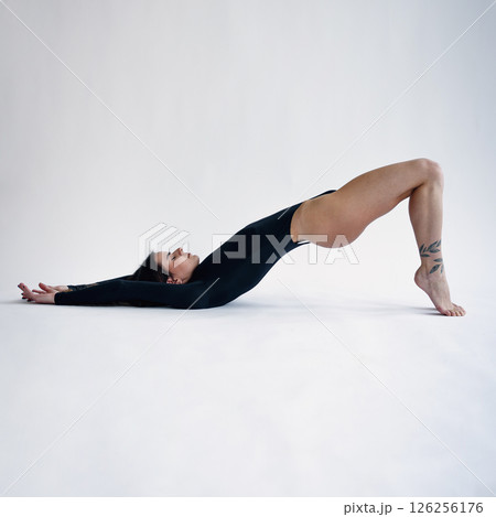 Attractive girl with perfect body in black bodysuit lies on back, arched at waist, leaning on toes Attractive girl with perfect body in black bodysuit lies on back, arched at waist, leaning on toes 126256176