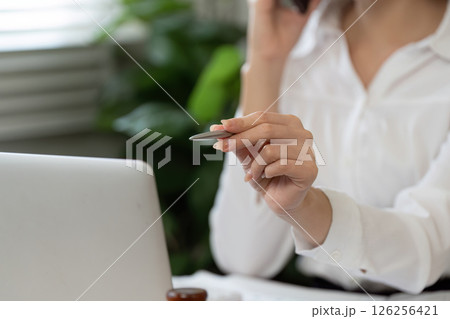Professional woman engaged in a phone conversation while reviewing financial documents in her office. 126256421