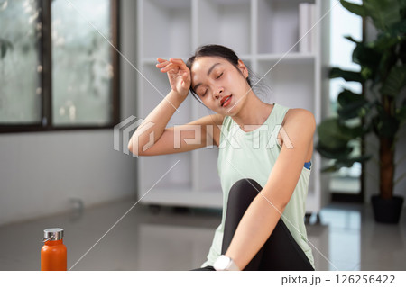 Exhausted young woman resting after workout, wiping sweat and hydrating with water bottle 126256422