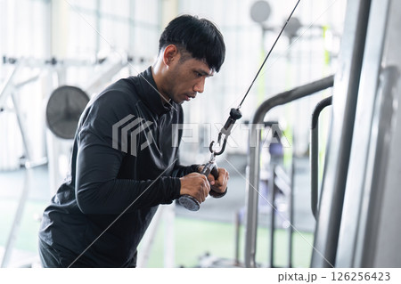 Workout and Fitness. Young man using cable machine for strength training in gym. 126256423