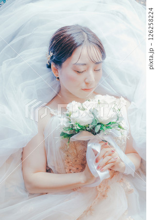 純白のドレスをまとい、ブーケを胸元に持って横たわる女性のイメージ写真 純白のドレスをまとい、ブーケを胸元に持って横たわる女性のイメージ写真 126258224