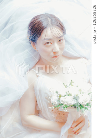 純白のドレスをまとい、ブーケを胸元に持って横たわる女性のイメージ写真 126258226