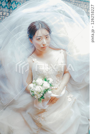 純白のドレスをまとい、ブーケを胸元に持って横たわる女性のイメージ写真 126258227