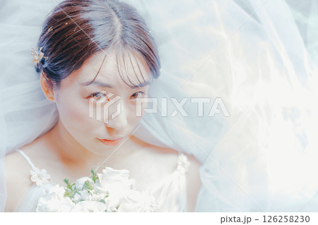 純白のドレスをまとい、ブーケを胸元に持って横たわる女性のイメージ写真 126258230