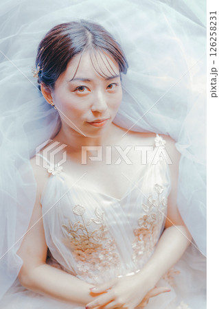 純白のドレスをまとい、ブーケを胸元に持って横たわる女性のイメージ写真 126258231