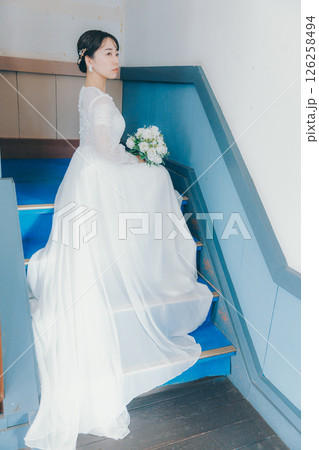 階段に座って振り返るウェディングドレス姿の女性のポートレート 階段に座って振り返るウェディングドレス姿の女性のポートレート 126258494