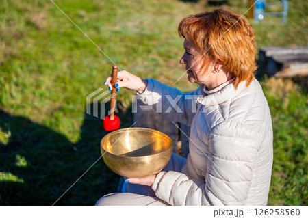 Woman playing a Tibetan singing bowl by a mountain river in Altai. Concept of sound healing, spiritual alignment, and deep connection with natural elements 126258560