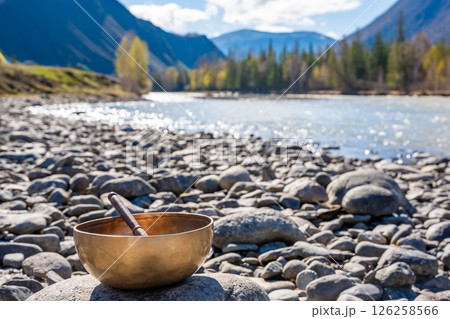 Tibetan singing bowl placed on river stones near mountain water in Altai. Concept of grounding energy, sacred silence, and spiritual resonance in wild nature 126258566