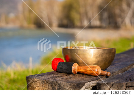 Tibetan singing bowl resting on a wooden bench by the Altai river. Concept of sacred stillness, energy resonance, and spiritual presence in untouched nature. 126258567