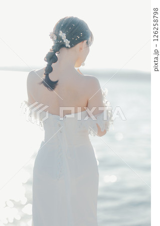 海辺の逆光に浮かぶウェディングドレス姿の女性のポートレート 126258798