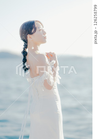 海辺の逆光に浮かぶウェディングドレス姿の女性のポートレート 126258799