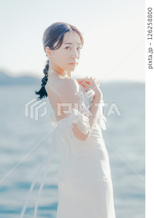 海辺の逆光に浮かぶウェディングドレス姿の女性のポートレート 126258800