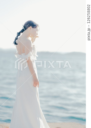 海辺の逆光に浮かぶウェディングドレス姿の女性のポートレート 126258802