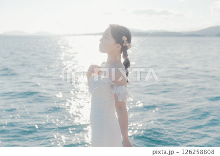 海辺の逆光に浮かぶウェディングドレス姿の女性のポートレート 126258808