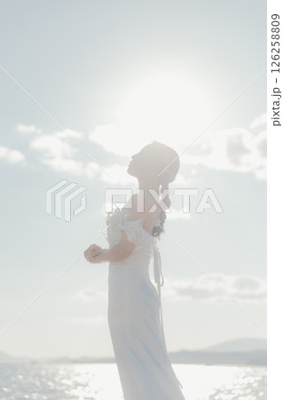 海辺の逆光に浮かぶウェディングドレス姿の女性のポートレート 海辺の逆光に浮かぶウェディングドレス姿の女性のポートレート 126258809