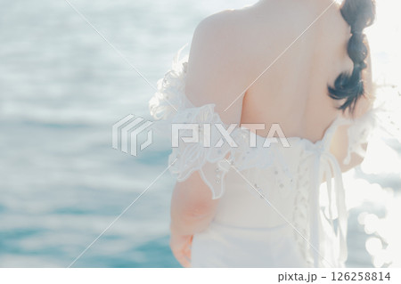 海辺の逆光に浮かぶウェディングドレス姿の女性のポートレート 126258814