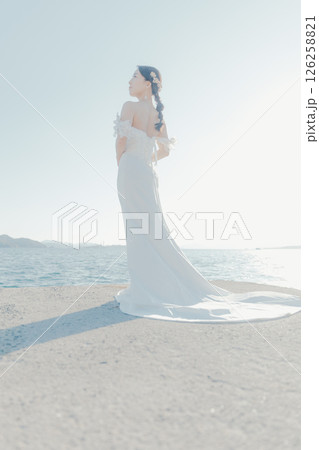 海辺の逆光に浮かぶウェディングドレス姿の女性のポートレート 126258821