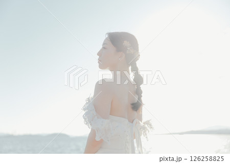 海辺の逆光に浮かぶウェディングドレス姿の女性のポートレート 海辺の逆光に浮かぶウェディングドレス姿の女性のポートレート 126258825