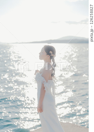 海辺の逆光に浮かぶウェディングドレス姿の女性のポートレート 126258827