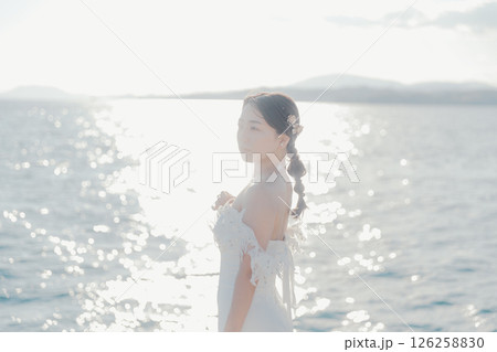 海辺の逆光に浮かぶウェディングドレス姿の女性のポートレート 126258830