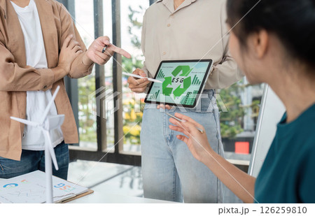 Innovative ESG Solutions. Team discussing sustainability strategies with digital tools in a modern workspace. 126259810