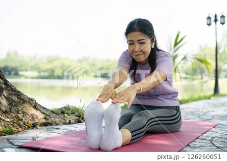 Wellness through Stretching. A woman practicing yoga outdoors by a serene lake. 126260051