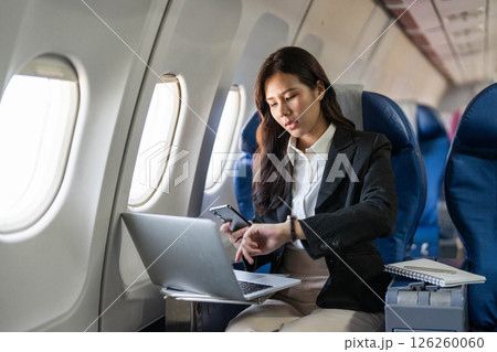 Business travel: Professional woman checking time on smartphone during flight Business travel: Professional woman checking time on smartphone during flight 126260060