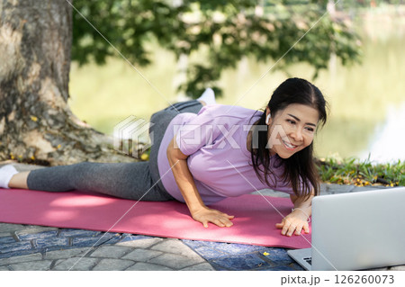Wellness and Yoga. A woman smiling while practicing yoga outdoors, embracing fitness. 126260073