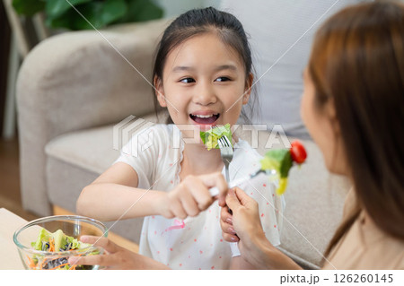 Wellness through sharing: Girl feeding salad to her mother 126260145