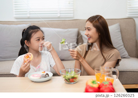 Wellness and healthy eating: Mother playfully feeding daughter a salad Wellness and healthy eating: Mother playfully feeding daughter a salad 126260325