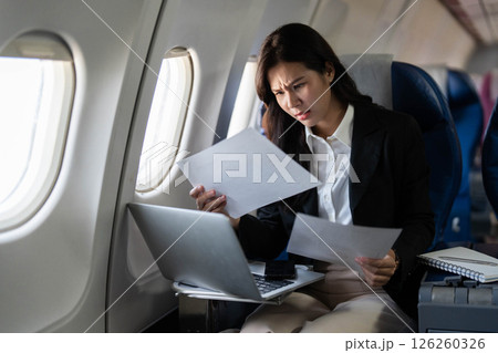 Business travel: Concerned professional woman evaluating documents on airplane Business travel: Concerned professional woman evaluating documents on airplane 126260326