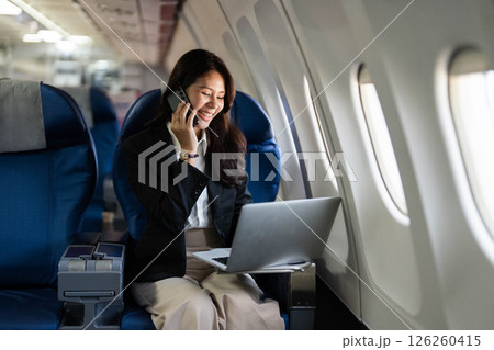 Business travel with a young professional woman working on a laptop and talking on the phone in an airplane 126260415