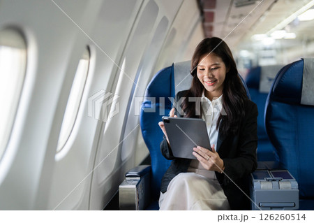 Business travel with young woman smiling while using tablet on airplane 126260514