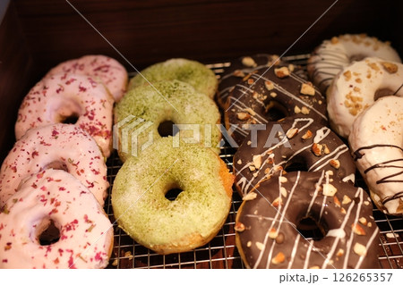 Color donuts in box on wood table from top view. variety of colorful donuts arranged in a box, featuring a mix of glazed, chocolate-coated, and sprinkled toppings. The assortment includes donuts 126265357
