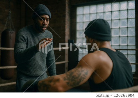 Instructions in boxing gym, experienced trainer instructs athlete developing sparring strategy, background of gym in retro style, gestures of trainer explain training strategy, moment of mentoring 126265904