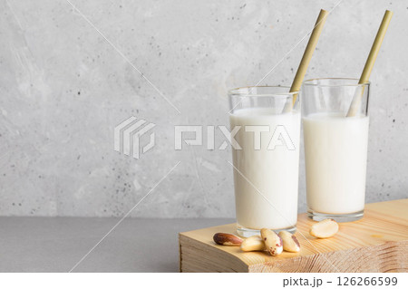 Brazil nut milk in two glasses with bamboo straws on wooden surface against textured background 126266599