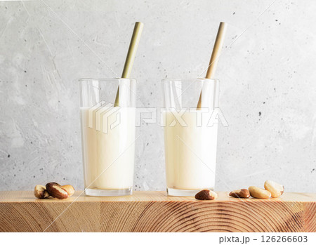 Brazil nut milk in clear glasses with bamboo straws on wooden surface against textured background 126266603