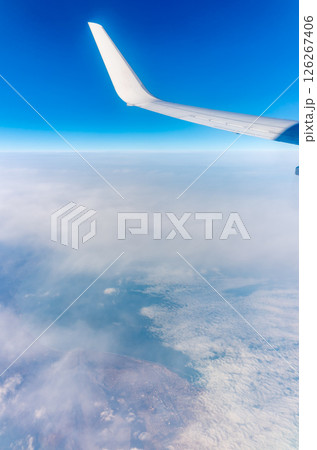 View from the airplane window at a beautiful blue clear sky, earth, sea and the airplane wing 126267406