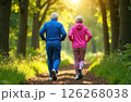 Gray-haired grandparents in pink and blue tracksuit jogging in the park, in the background in blurred green trees 126268038