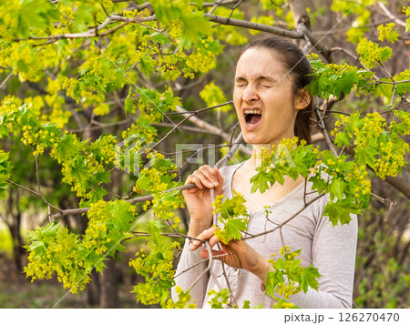 Young woman sneezes in the park against the background of a flowering tree. Allergy to pollen concept. 126270470