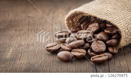 Close up of Roasted Coffee Beans Spilling from a Burlap Sack on Rustic Wooden Surface 126270975