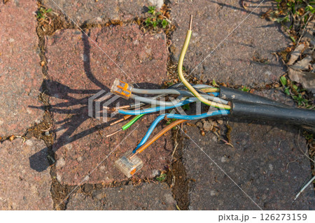 Frayed electrical cables exposed on rustic brick pavement. Colorful wires visible, highlighting potential safety hazard. Emphasizes need for cable repair or replacement. 126273159